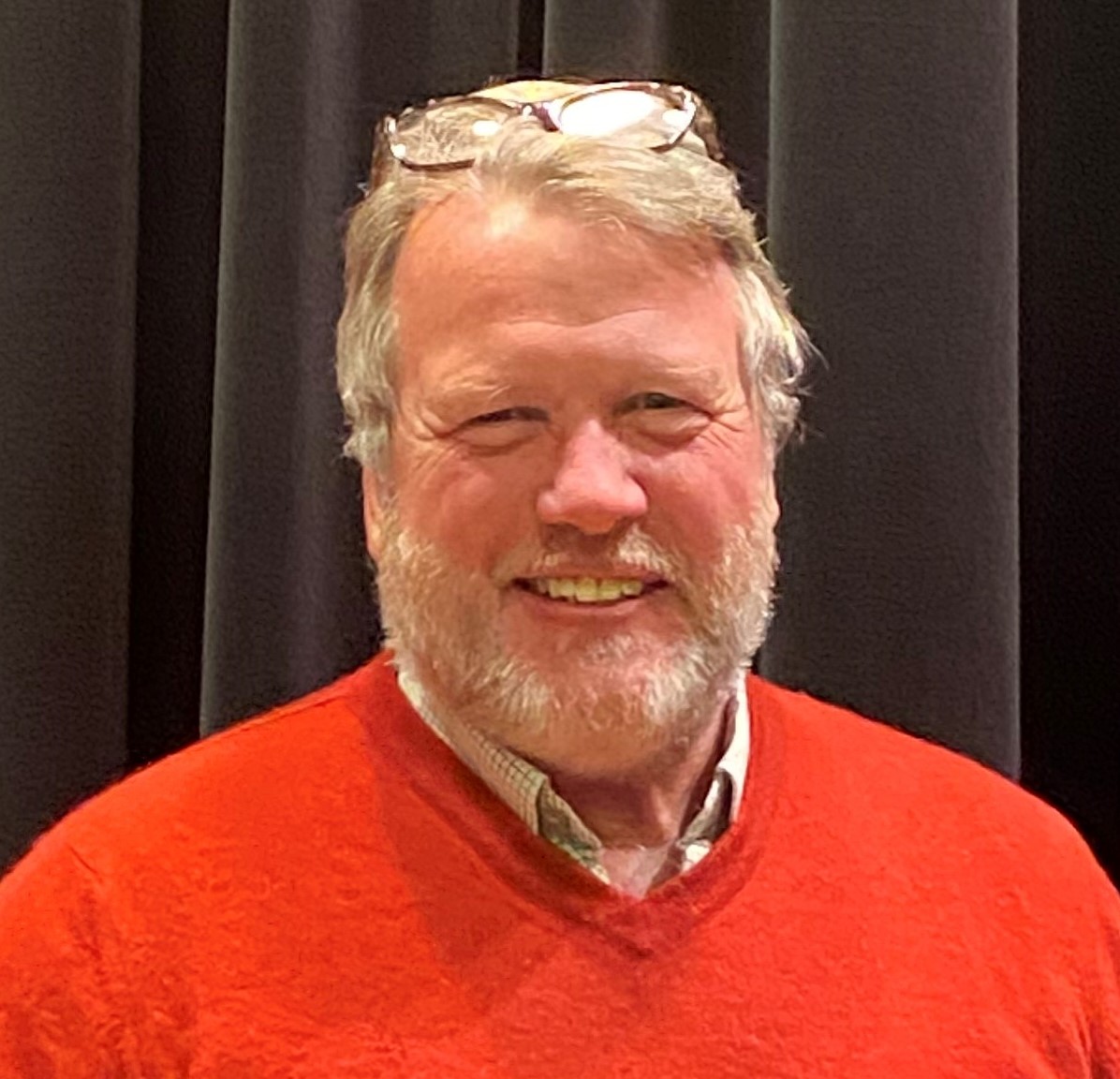 a smiling man with a beard wears a red sweater